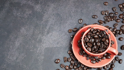 Roasted coffee beans in a red cup on black background.