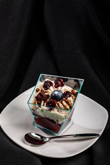One-person portion of layered dessert in trapezoid glass on white plate, isolated on dark fabric
