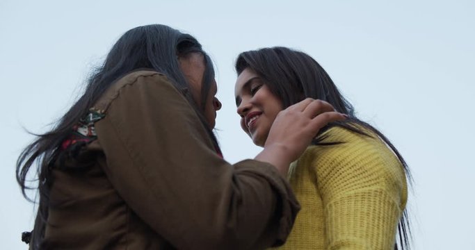 Low angle, looking up, two medium mid shot ms of two young attractive women dancing and swaying holding hands and staring with romantic love and passion against the blue sky slow-motion handheld 60fps