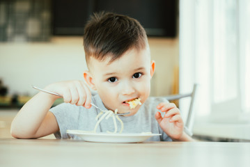 A child in the kitchen at the table eats macaroni and cheese very appetizing