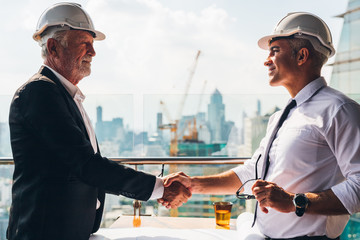 Two engineer wear safety helmet shaking hands after meeting for architectural project working with partner. Worker and customer having agreement in factory. Industry, Engineering, construction concept