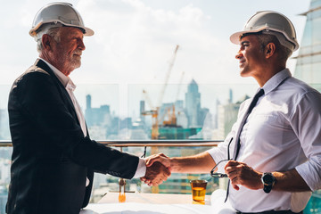 Two engineer wear safety helmet shaking hands after meeting for architectural project working with...