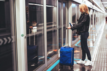 Adult lady stands with a suitcase in airport subway.
