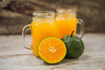 Naklejka na ściany i meble Orange juice and oranges with green peel on a wooden background