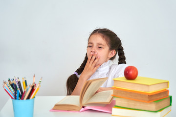 Child girl schoolgirl sitting at a Desk and yawning. Tired school and homework.