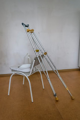 Crutches propped on the back of a chair where a urinal and a hospital duck stand. A ward in a...