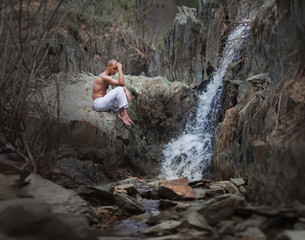 Buddhist. Bald man. Meditation in the mountains against the backdrop of a waterfall. Prayer.