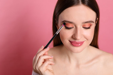 Fototapeta premium Beauty blogger applying eyeshadow on pink background, closeup