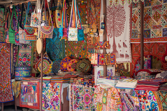 Vibrant, colorful market stall selling embroidered handicrafts such as pillow cases, tote bags, and blankets