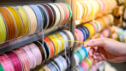 Male hand choosing Yellow Ric Rac ribbon from colorful ribbon rack in craft shop. Artisan and...