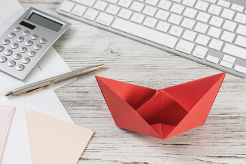 Businessman workspace at desk with red paper ship