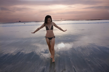 Fototapeta premium A woman in a bikini walking on a lonely Thailand beach. at sunset