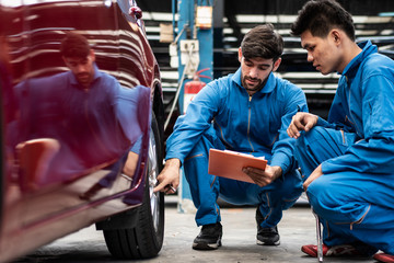 automotive mechanic men checking at  car tyre rubber condition needed for replacement, man pointing hand at wheel following maintenance checklist document, after service at auto repair shop concept © winnievinzence