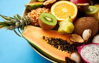 food, summer and healthy eating concept - close up of plate of different exotic fruits on blue background
