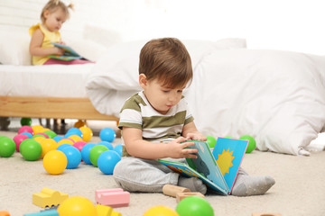 Cute little boy with book playing on floor while girl sitting on bed. Children's development