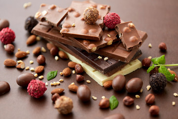 sweets, confectionery and food concept - close up of different chocolate bars, candies and nuts on brown background