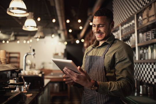 Portrait of successful young afro-american cafe owner standing behind counter using digital tablet - Powered by Adobe