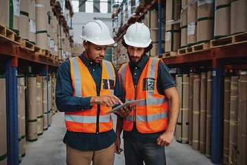 Young focused workers in warehouse discussing work on digital tablet