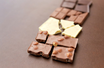 sweets, confectionery and food concept - milk, dark and white chocolate bars on brown background