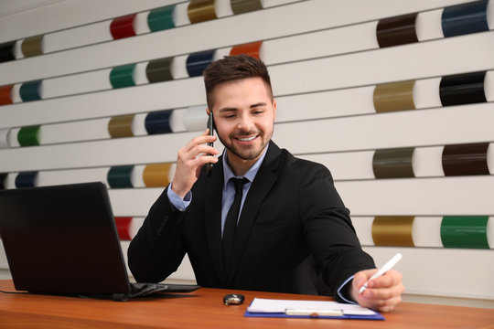 Salesman Talking On Phone At Desk In Car Dealership