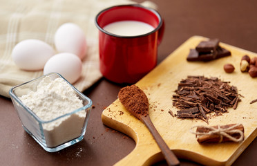 confectionery and culinary concept - chocolate, cocoa powder, hazelnuts with milk, eggs and flour on brown background