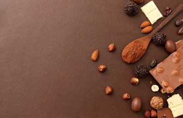 confectionery and food concept - milk, dark and white chocolate bars with nuts, candies, cocoa beans and powder on brown background