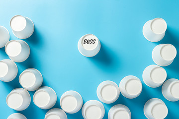 One cup is surrounded by paper cups for drinks on a blue background. Concept friendly team, leader, director, boss. Banner. Flat lay, top view