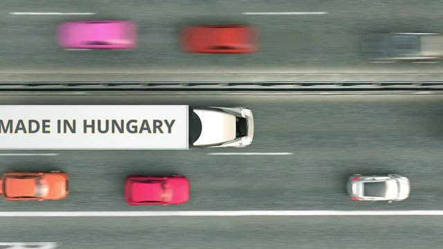 Aerial top down view of semi-trailer trucks with MADE IN HUNGARY text driving along the road. Hungarian business related loopable 3D animation