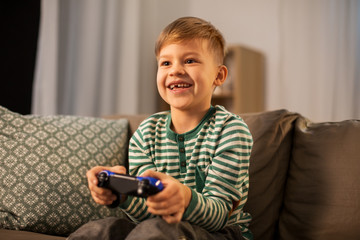 leisure, technology and people concept - happy little boy with gamepad playing video game at home...