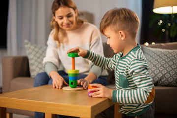 family, leisure and people concept - happy smiling mother and son playing with toy pyramid at home in evening