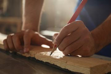 Professional carpenter making mark on wooden board in workshop, closeup