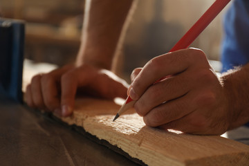 Fototapeta na wymiar Professional carpenter making mark on wooden board in workshop, closeup