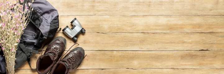 Boots for trail, backpack, binoculars, camping equipment on a wooden background. The concept of hiking, tourism, camp, mountains, forest. Banner. Flat lay, top view