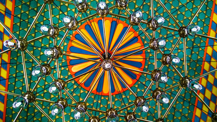 Oriental ceiling in different colors with colorful ornaments in green colors and large chandelier hanging, an interesting eastern design of the building interior