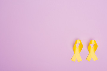 Flat lay with yellow awareness ribbons on violet background, international childhood cancer day concept