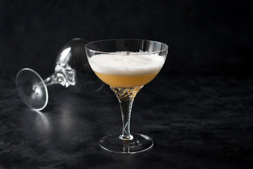 Whiskey Sour cocktail is a mixed drink containing whiskey (usually bourbon), lemon juice and sugar, with a small amount of egg white. Two crystal glasses on a black background.