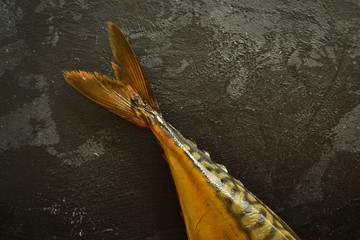 Tail of smoked fish. Mackerel tail on a dark background, place for text, top view, dark background.