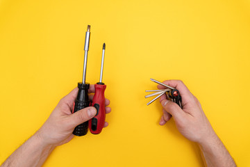 Two different screwdrivers in left male hand and multitool in right mans hand, compare, vs, minimal concept., yellow background. Copy space.