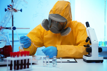 Scientist in chemical protective suit dripping reagent on microscope slide at laboratory. Virus...