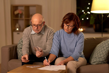 family, savings and people concept - smiling senior couple with bills counting money at home