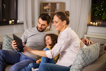 family, people and technology concept - happy smiling father, mother and little daughter with tablet pc computer at home at night