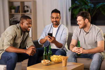 friendship, leisure and people concept - male friends with smartphone drinking beer at home at night