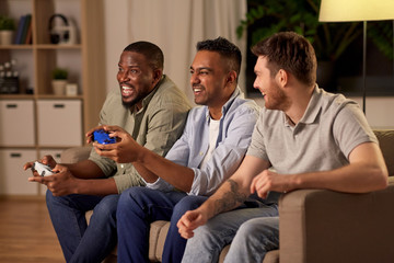 friendship, technology and leisure concept - smiling male friends with gamepads and beer playing...