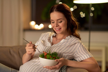 pregnancy, healthy food and people concept - happy smiling pregnant woman eating vegetable salad at home