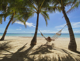 Girl resting,swinging on hammock in paradise resort.Beautiful sandy white beach with sea, palm trees. Shadows on sand