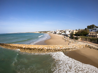 Aerial recording overlooking the horizon, waves breaking against the breakwater, Mediterranean sea, green and clear water, clear blue sky, low tide in the port of Santa Maria, Cádiz, Andalusia. © DavidRojasS