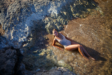 Beautiful girl in a swimsuit lies on a sandy beach in sea water