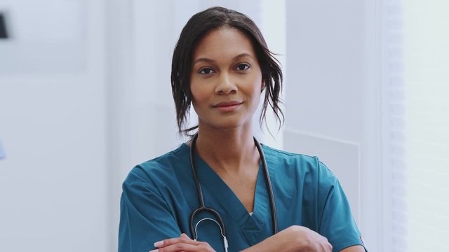 Portrait Of Female Doctor With Stethoscope Wearing Scrubs In Busy Hospital Corridor 