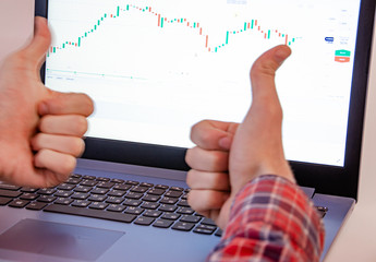 Trading on the exchange. Men's hands in a plaid shirt behind a laptop thumb up and down. rates, promotions. Win, lose. Good luck and failure in trade. Focus on laptop and  graphics