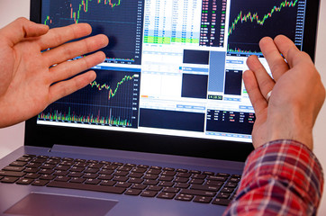 Trading on the exchange Men's hands in a plaid shirt behind a laptop show on the graph. On-screen...